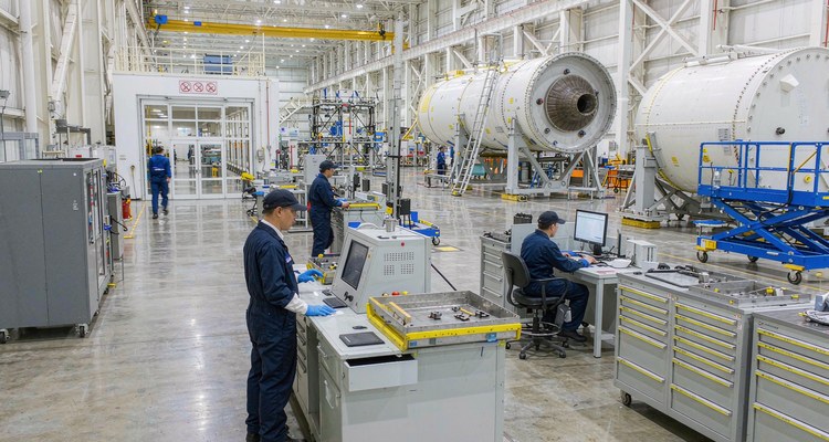 Digital weighing and check-in station with tool cabinets in an aerospace MRO hangar, with recovered rocket boosters on stands behind