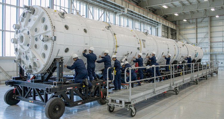 Recovered rocket first-stage booster on a horizontal integration stand with a mobile work platform during refurbishment